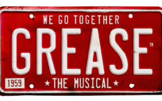 A red, vintage-style number plate with white text that reads, "WE GO TOGETHER GREASE THE MUSICAL." In the bottom left corner, there is a small rectangle with "1959" inside it. The overall design promotes the musical "Grease.