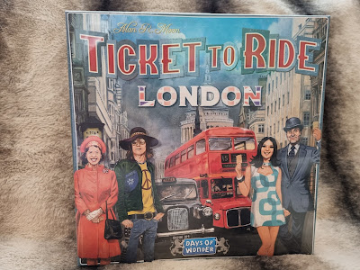 The cover of the board game "Ticket to Ride: London" shows four people in 1960s attire standing by a red double-decker bus with Big Ben and other London landmarks in the background. The title is boldly displayed above them.