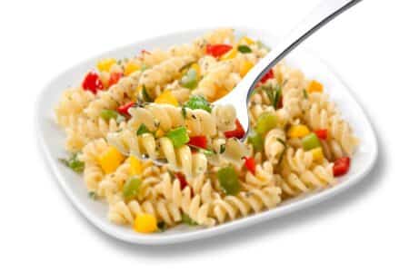 A square white plate holds rotini pasta mixed with diced yellow, red, and green peppers, and herbs. A fork in the foreground lifts a serving, showing the colourful vegetables and spiral pasta in detail.