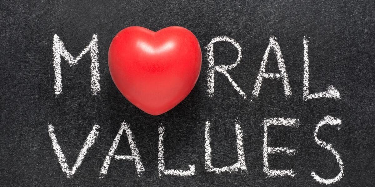 A red heart replaces the letter "O" in the word "MORAL," which, along with the word "VALUES," is written in white chalk on a blackboard, symbolising moral values connected with love, care, and compassion.