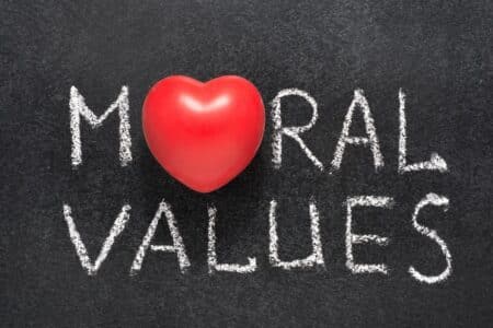 A red heart replaces the letter "O" in the word "MORAL," which, along with the word "VALUES," is written in white chalk on a blackboard, symbolising moral values connected with love, care, and compassion.