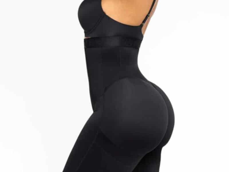 A woman is shown from the side, wearing a black high-waisted body shaper that extends to mid-thigh, with a fitted design to smooth and contour her figure. The background is plain white, highlighting the shapewear.