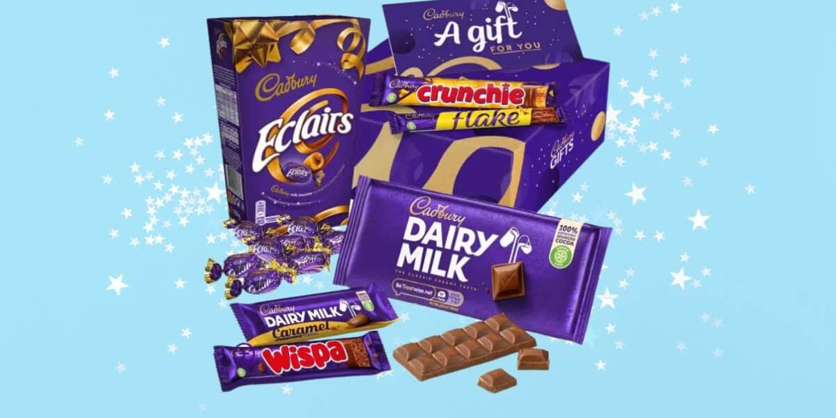 A selection of Cadbury chocolates, including Dairy Milk, Wispa, Flake, Crunchie, Éclairs, and other treats, displayed in and around a purple gift box on a light blue background with white star-like sparkles.