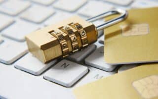 A gold combination padlock lies on a white computer keyboard beside two gold credit cards, symbolising online security and protection of financial data.
