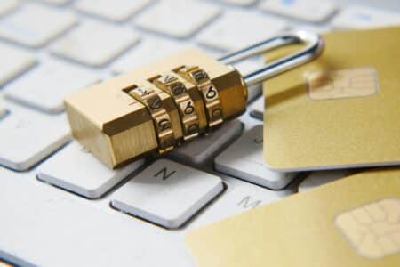 A gold combination padlock lies on a white computer keyboard beside two gold credit cards, symbolising online security and protection of financial data.